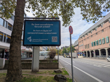 Bild einer Infotafel im Stadtgebiet von Koblenz. Der Text der Tafel lautet: "Du hast sexualisierte Gewalt erlebt? Du hast ein Recht auf Unterstützung und Beratung!" Autonome Frauennotrufe in Rheinland-Pfalz mit QR Code